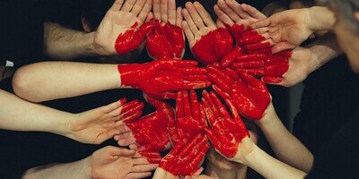 Mehrere Menschen halten ihre Handflächen aneinander, auf die mit roter Farbe ein Herz aufgemalt wird